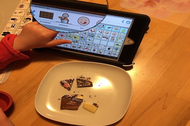Ein M&auml;dchen m&ouml;chte Schokolade probieren. Das M&auml;dchen findet die Schokolade fein. Sie zeigt deshalb die drei Bilder f&uuml;r: 1. Schokolade, 2. probieren und 3. lecker auf einem Tablet.