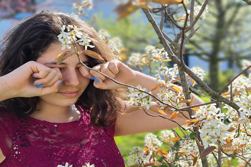 Ein Mädchen ist im Garten. Es hat viele Pollen in der Luft. Das Mädchen reibt sich die Augen. Die Augen brennen und tränen. Sie hat Heuschnupfen.