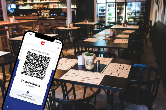 Bildmontage: Im Hintergrund ist ein Restaurant mit gedeckten Tischen zu sehen. Links vorne eine Handygrafik mit dem Covid-Zertifikat.