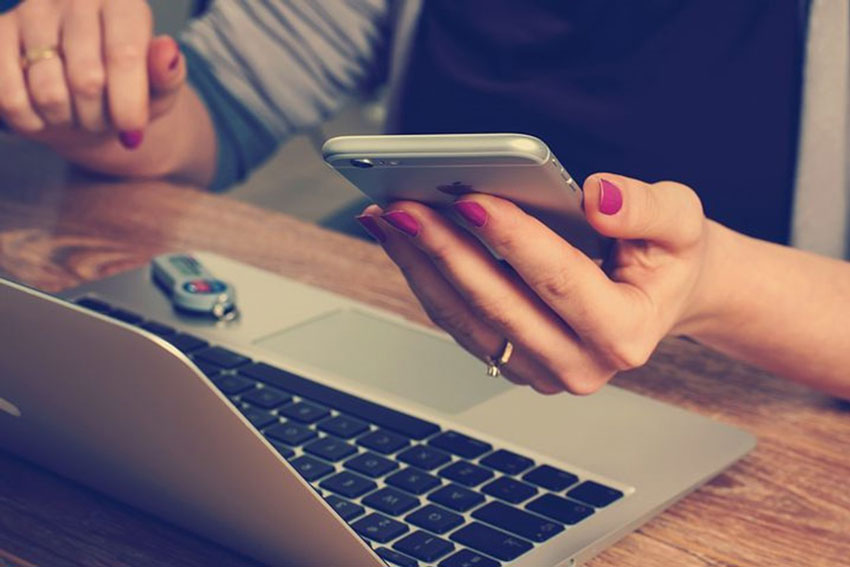 Eine Frau löst am Laptop Hausaufgaben. Gleichzeitig hält sie ihr Handy in der Hand.