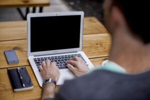 Ein Mann sitzt an einem Holztisch und arbeitet am Computer.