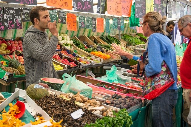 Menschen kaufen an einem Marktstand Gem&uuml;se und Fr&uuml;chten.