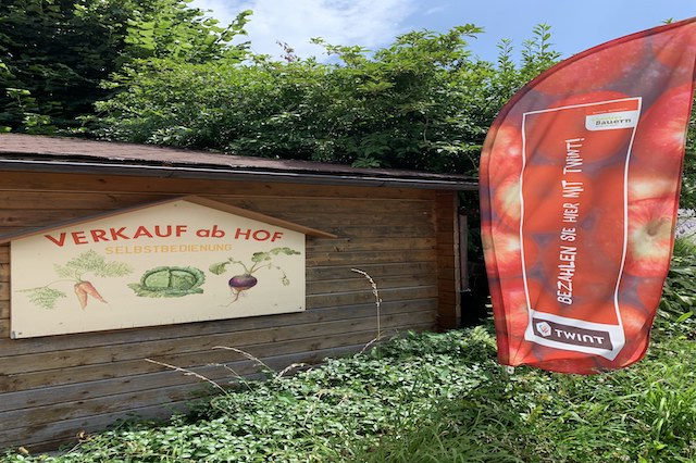 Ein Bauernhof wirbt mit einem Schild f&uuml;r seinen Hofladen. Neben dem Schild steht eine Fahne. Darauf steht: Bezahlen Sie hier mit TWINT.