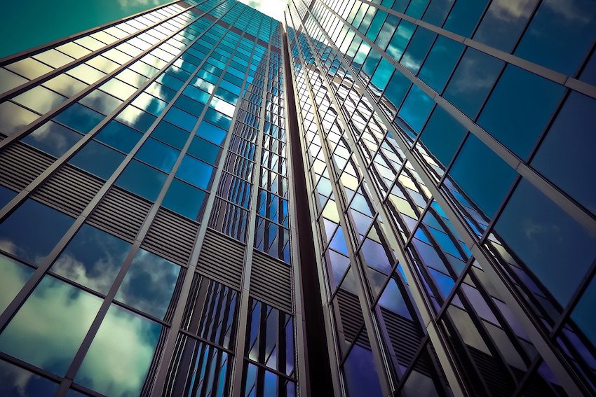 Das Bild zeigt ein Hochhaus mit einer Fassade aus lauter Fenstern. In den Fensterscheiben spiegeln sich Wolken.