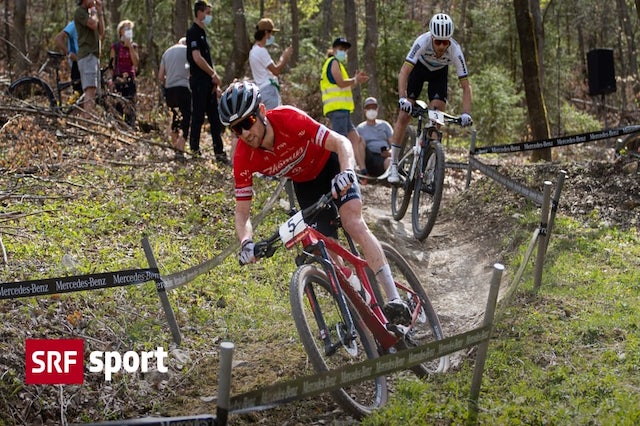 Mountain-Bike-Rennen: Zwei M&auml;nner sind auf einer Abfahrt auf einem schmalen, unebenen Weg. Der Weg f&uuml;hrt durch Wald und Wiesen.