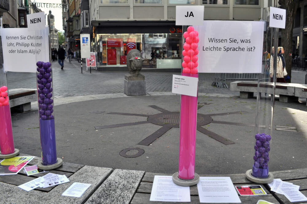 Vier R&ouml;hren aus Plexiglas stehen auf einer Bank. In zwei R&ouml;hren hat es rosa B&auml;lle, in den anderen zwei R&ouml;hren hat es violette B&auml;lle. Rosa steht f&uuml;r Ja, violett f&uuml;r Nein.