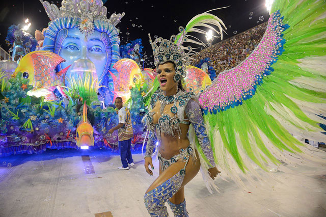 Karneval in Rio. Zuvorderst tanzt eine Frau mit grossen rosa, blauen und gr&uuml;nen Engelsfl&uuml;geln. Dahinter folgt ein bunter Wagen.