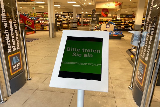 Bei Aldi steht beim Eingang ein Monitor. Bei Gr&uuml;n steht: Bitte treten Sie ein. Dann d&uuml;rfen die Kunden ins Gesch&auml;ft.