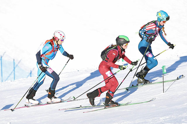 Drei Ski-Bergsteigerinnen laufen auf Ski mit Fellen den Berg hoch. Es ist ein Wettrennen.