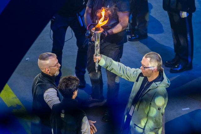 Rinaldo Burgener &uuml;bergibt die brennende Fackel an zwei Sportler.