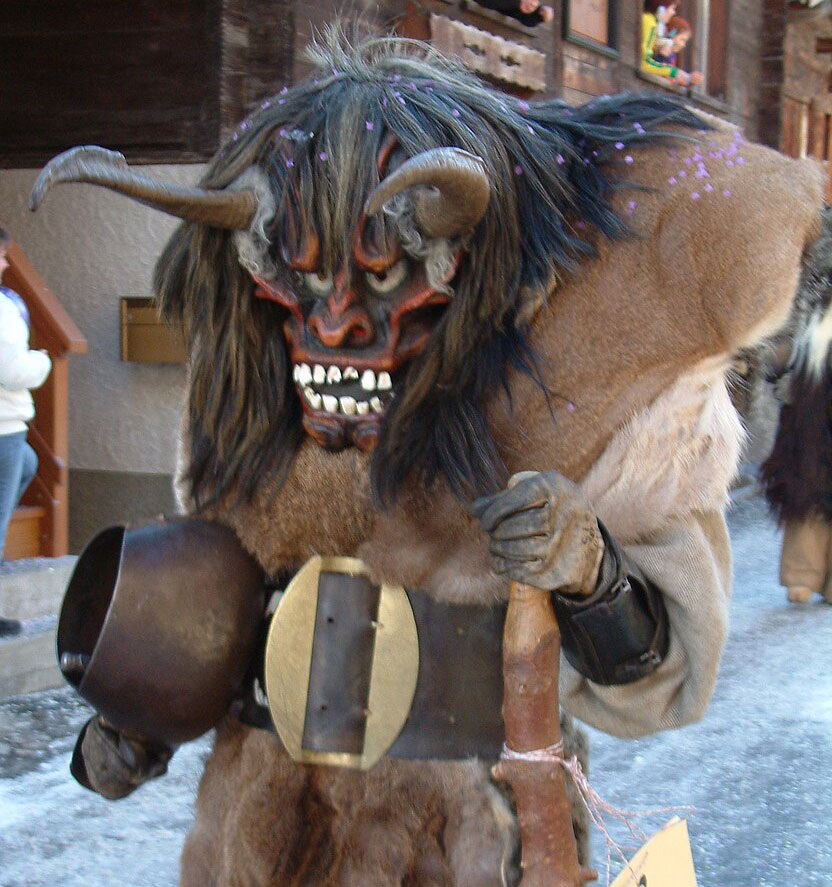 Ein Tsch&auml;gg&auml;tta mit einer grossen gruseligen Maske aus Holz mit grossen Z&auml;hnen und gekr&uuml;mmten H&ouml;rner. Er tr&auml;gt ein Umgang aus Fell und einen breiten G&uuml;rtel. Am G&uuml;rtel h&auml;ngt eine Schelle.