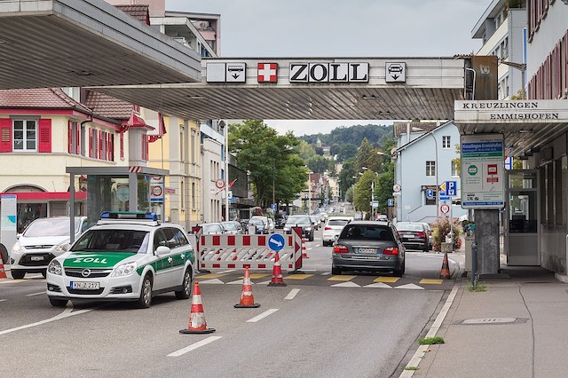 Ein Auto f&auml;hrt &uuml;ber den Zoll. Der &Uuml;bergang ist mit einem Dach bedeckt. Am Dach steht auf einem Schild Zoll. Links davon ist das Schweizer Wappen.