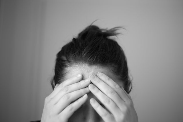 Eine Frau st&uuml;tzt mit beiden H&auml;nden ihren Kopf. Die H&auml;nde liegen auf der Stirn und verdecken die Augen.