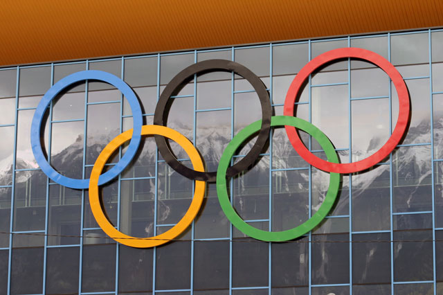 Die olympischen Ringe hangen vor einer grossen Fensterfront.
