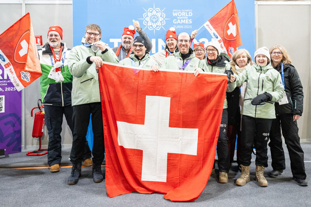 Das Schweizer Team steht vor dem Siegerpodest und h&auml;lt eine Schweizer Flagge.