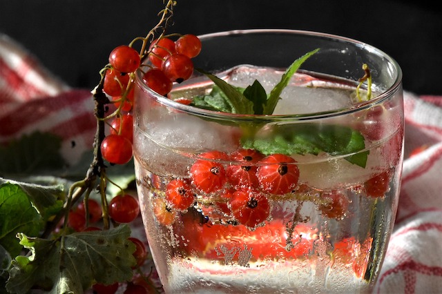 Ein Trinkglas mit Wasser, Eisw&uuml;rfeln und frischen Johannisbeeren